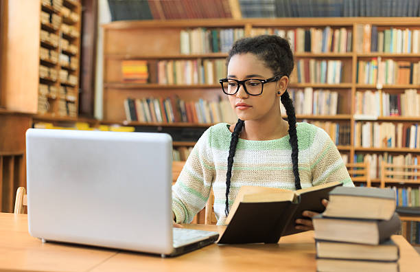 стокові фото, фото роялті-фрі та зображення на тему сконцентрована молода жінка за допомогою ноутбука в бібліотеці - remote learning college